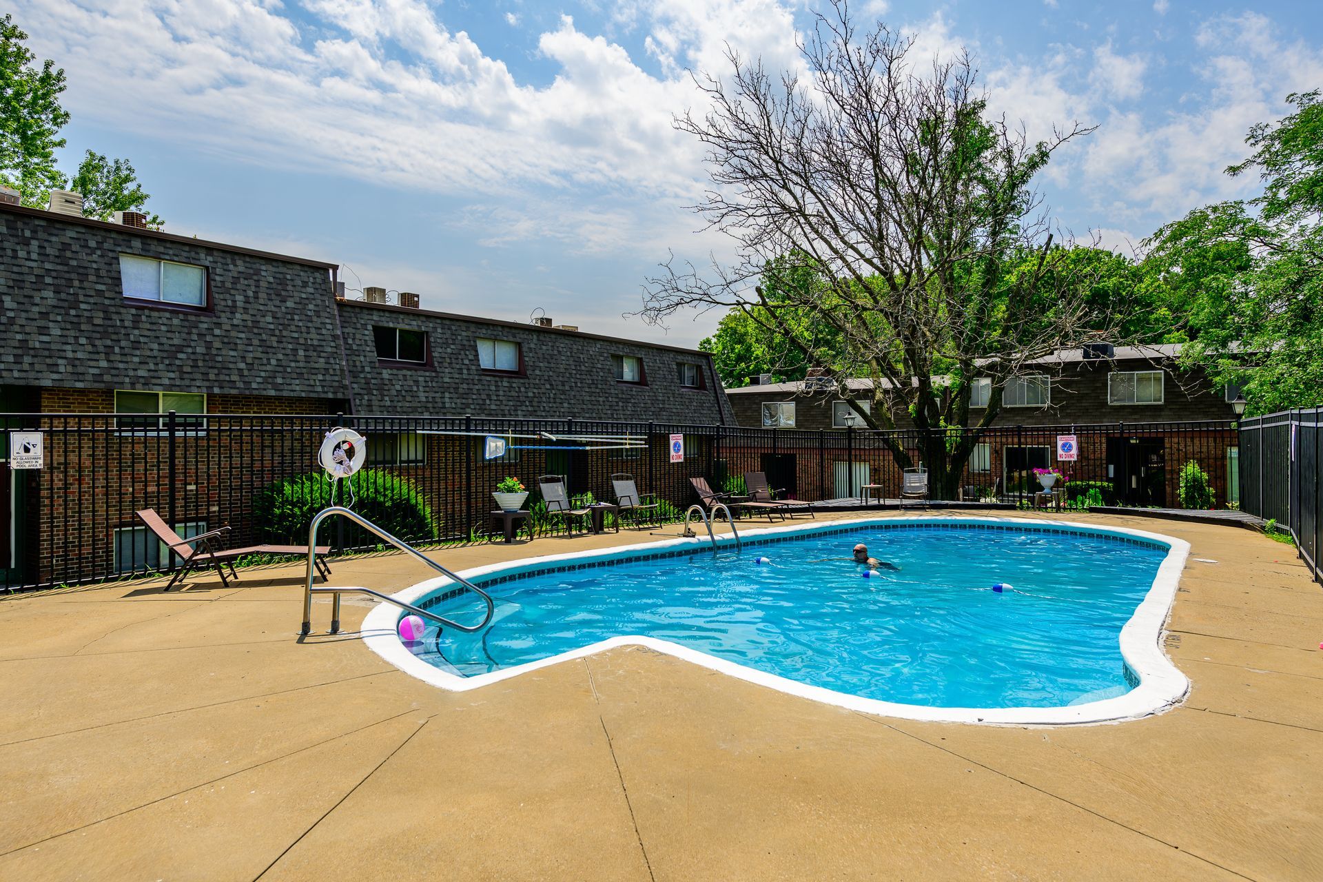 A large swimming pool is surrounded by a fence in front of a building.