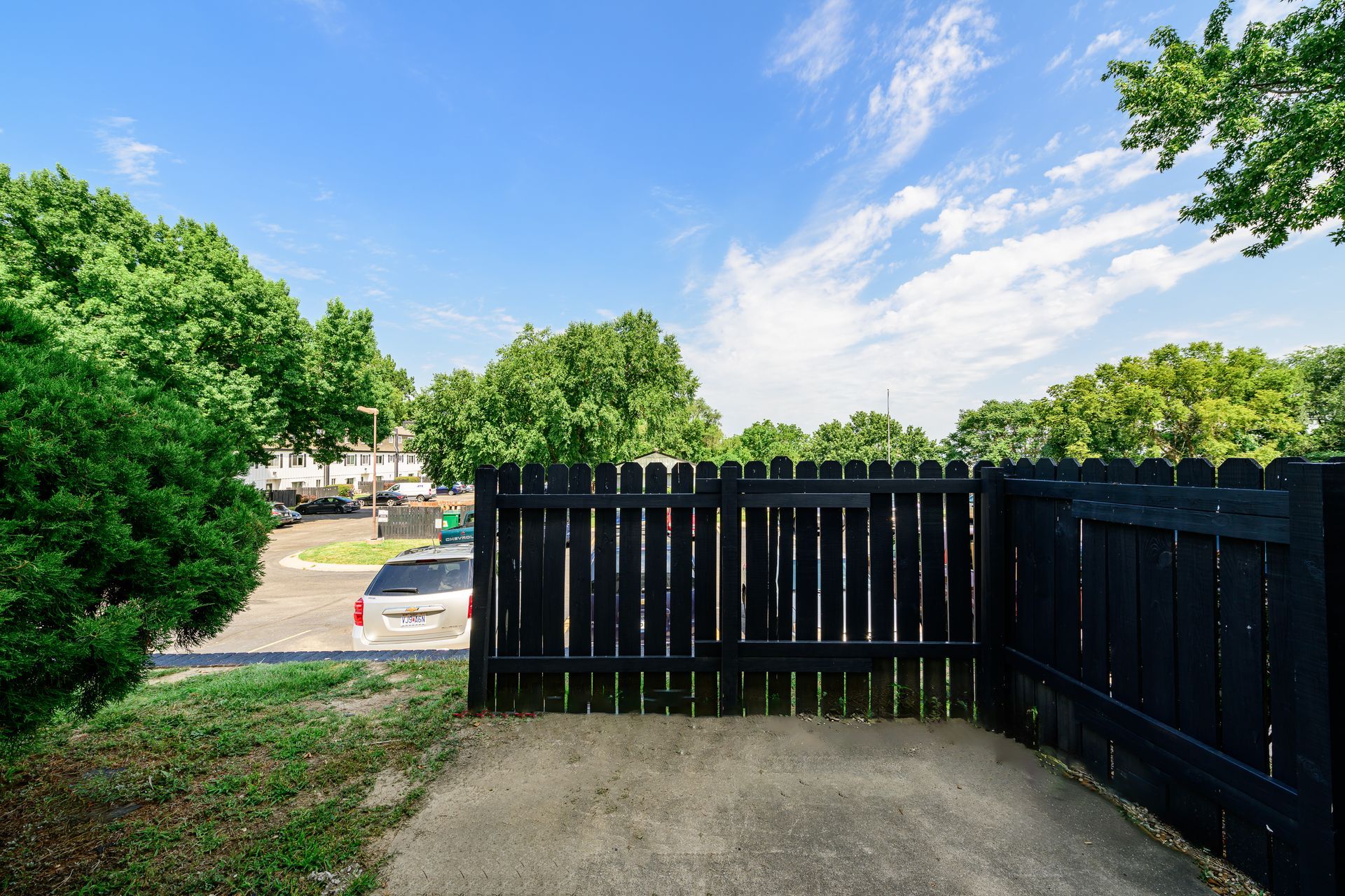 A black fence surrounds a parking lot with trees in the background