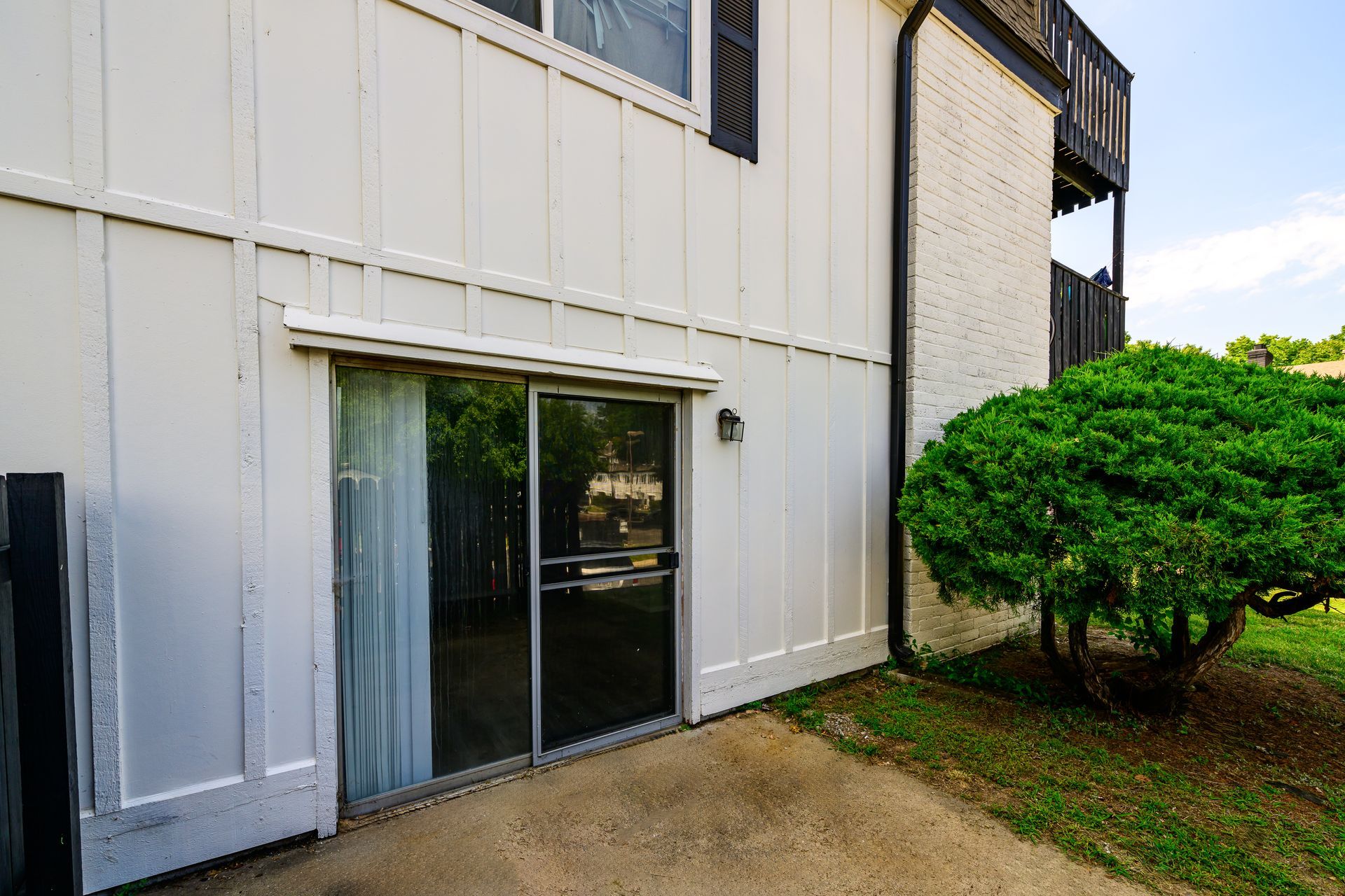 A white house with a sliding glass door and a tree in front of it.