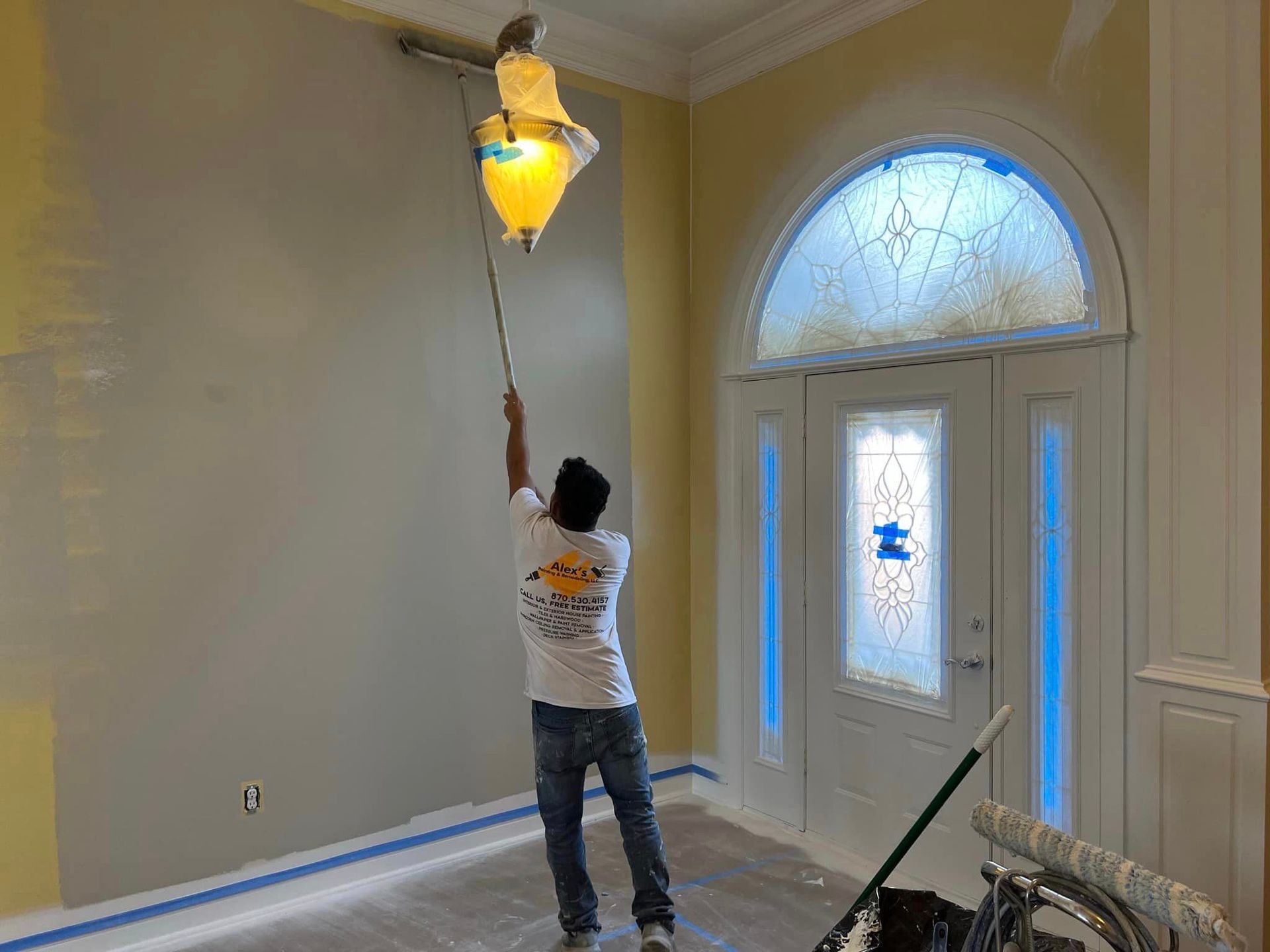 A man on the alex's painting & remodeling team is painting a wall with a roller in a living room.