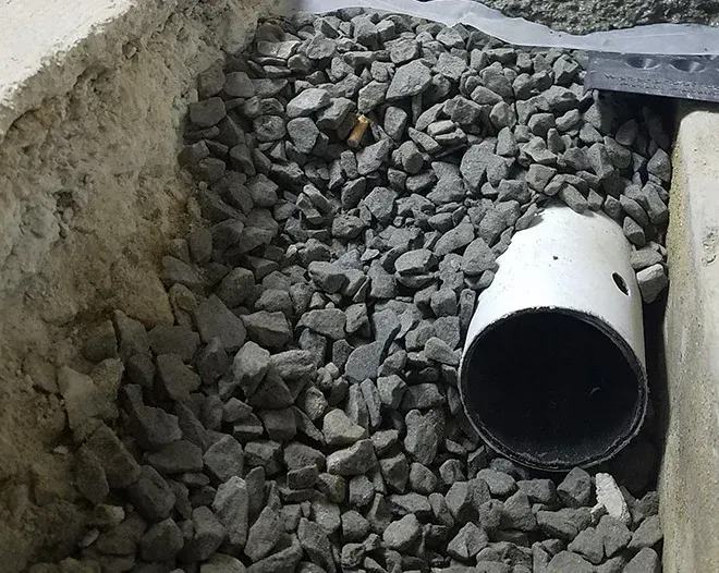White PVC pipe lying in a gravel trench beside concrete walls