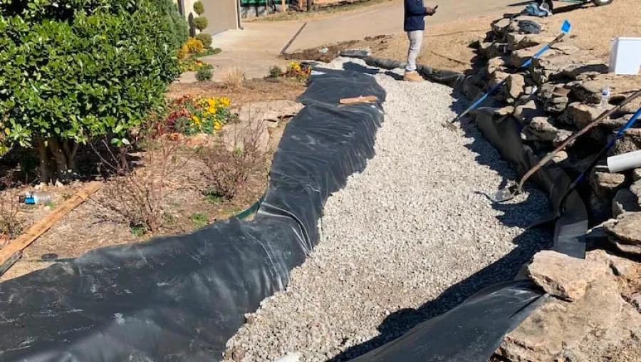 Curving gravel path bordered by black landscape fabric, rocks, and shrubs under construction