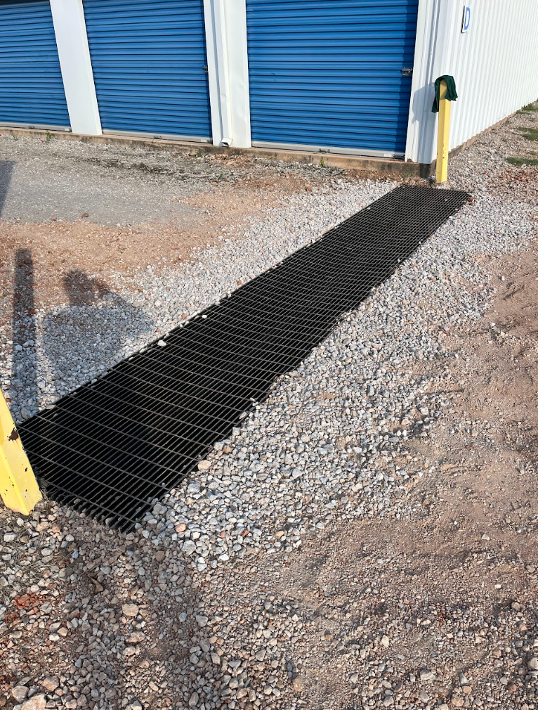 Gravel path with black drainage mat leading to blue storage unit doors