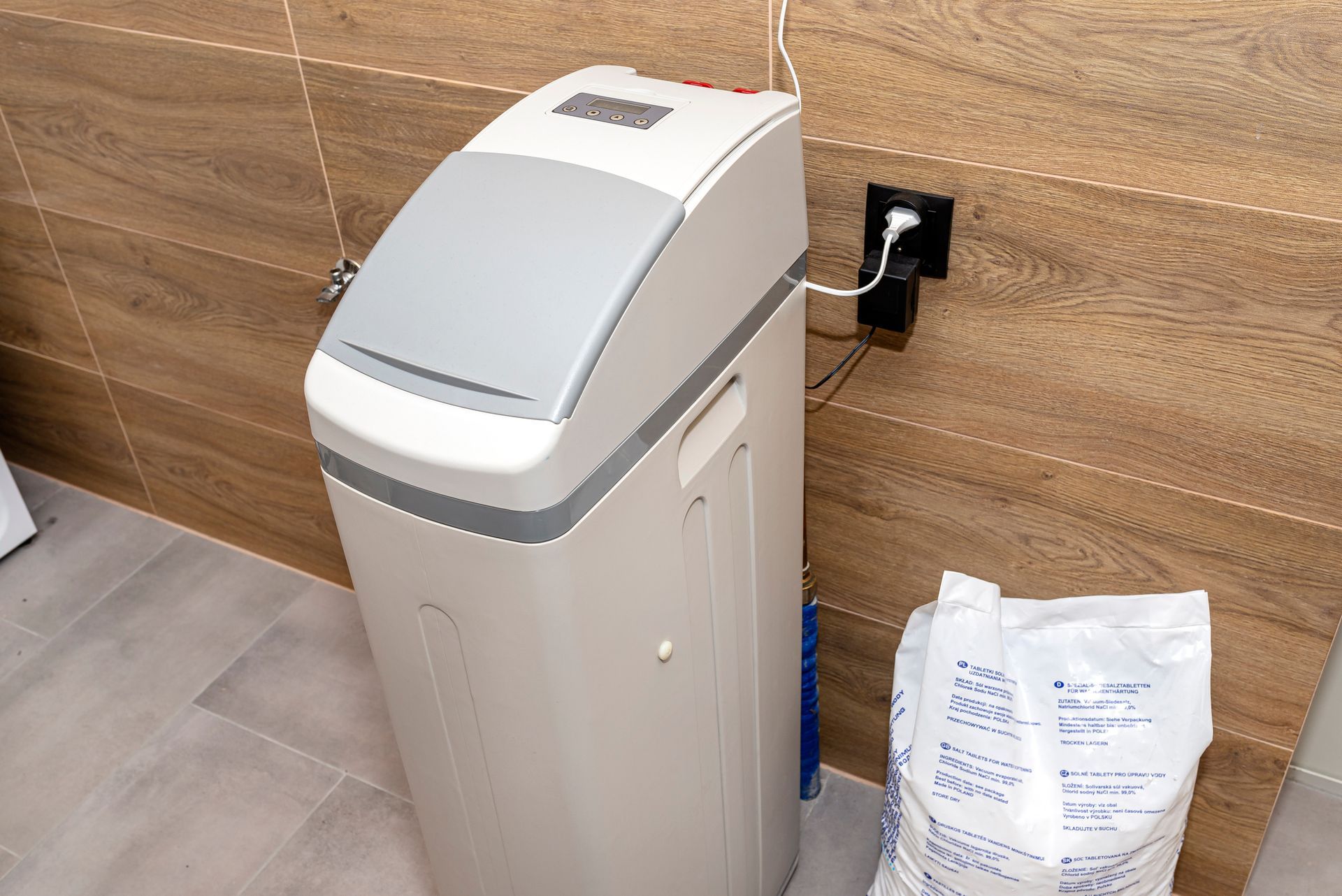 Water softener appliance in a tiled room, with a bag of salt beside it.