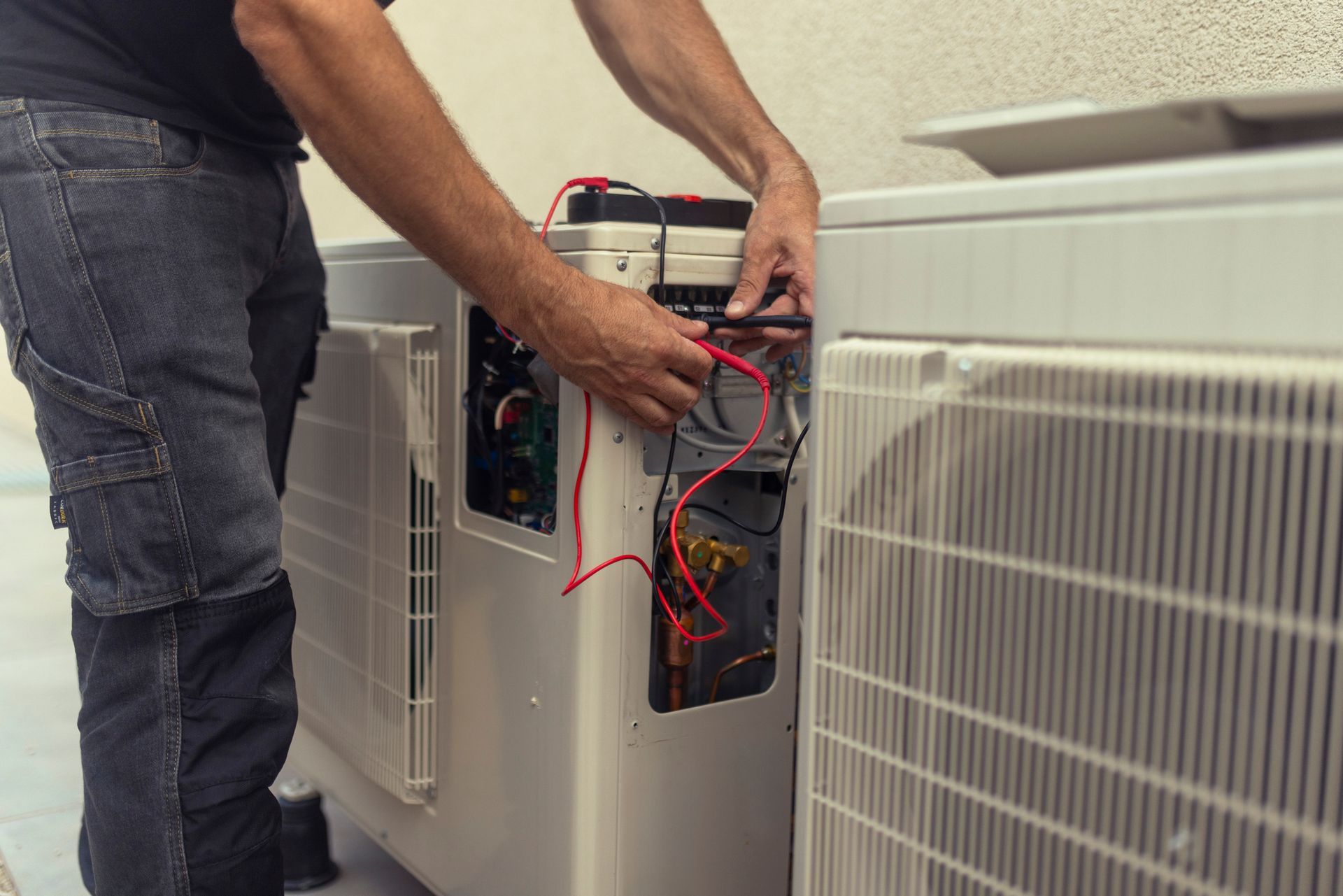 Person in jeans repairing air conditioner unit with tools outside.