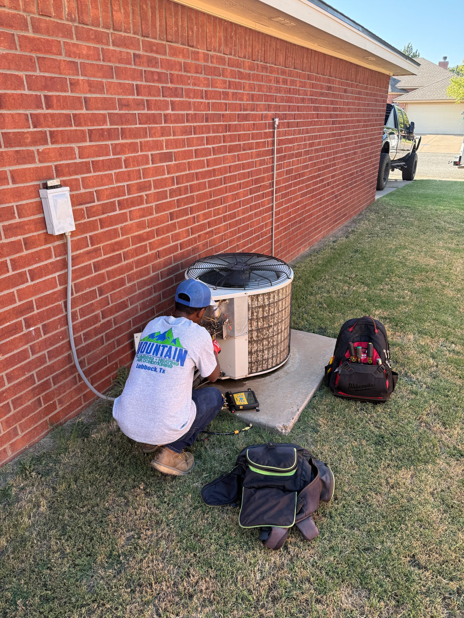 Air conditioning unit outside a building, brown siding, set on a concrete pad, surrounded by dark gravel.
