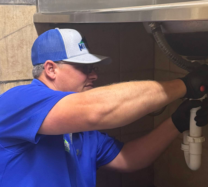 Person with wrench repairing plumbing under a sink.
