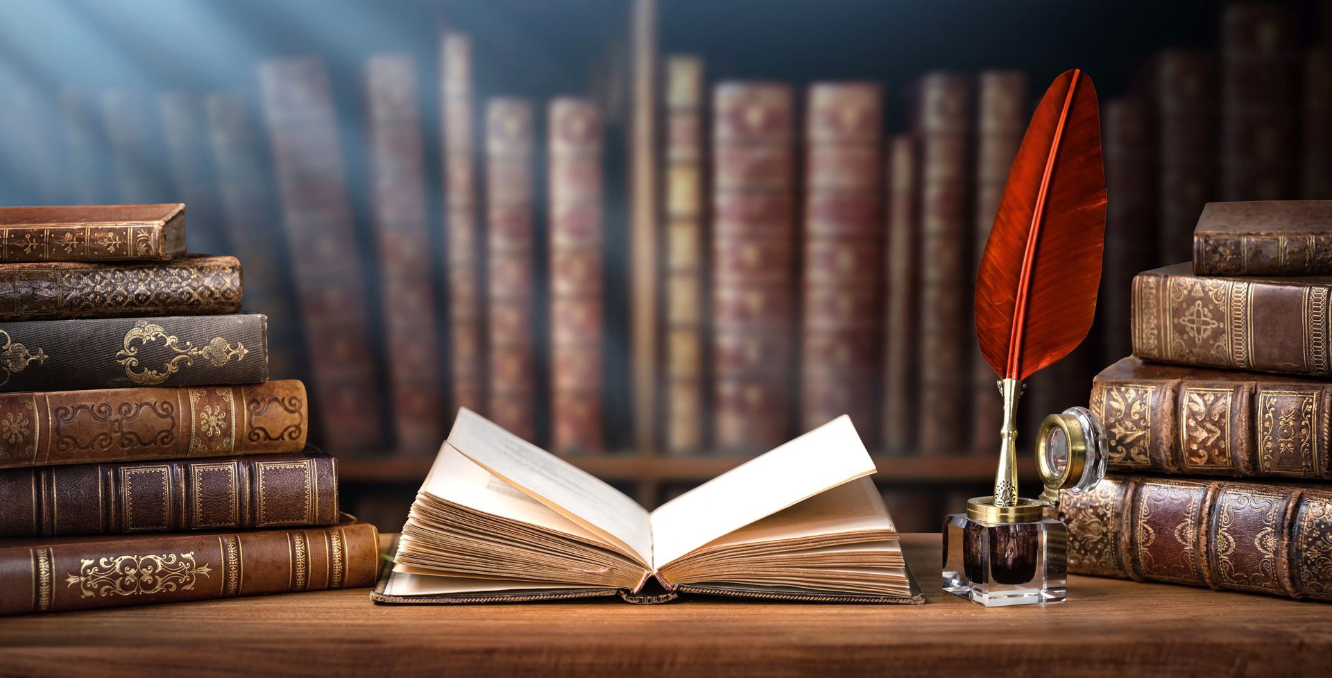 Open book on wooden desk with stacked old books and a red quill in a library setting