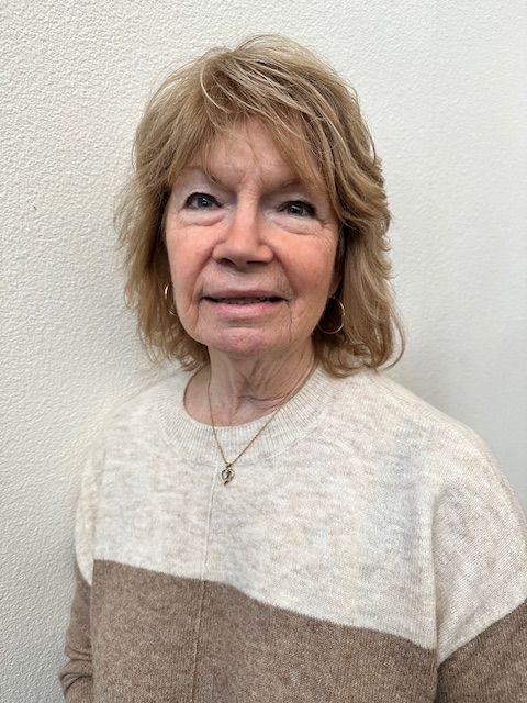 A woman wearing a white shirt and a necklace is smiling for the camera.