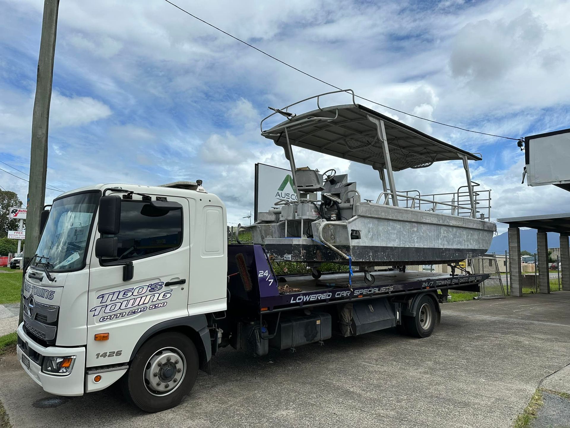 A white tow truck carries a silver boat with a canopy — Tigo’s Towing In Cairns City, QLD