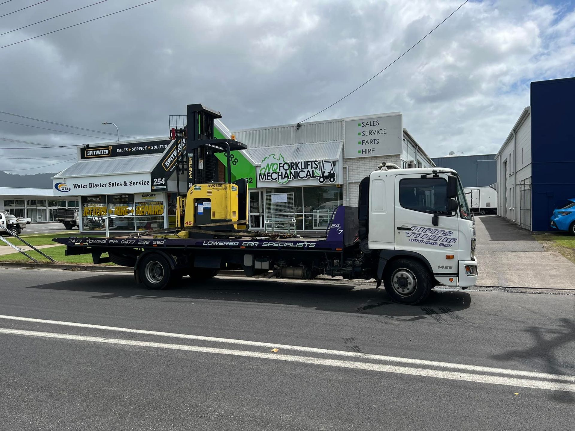 a Flatbed Truck Carrying a Yellow Forklift Parked — Tigo’s Towing In Cairns City, QLD