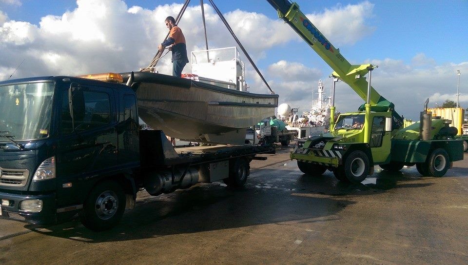a Small Boat Being Loaded Onto a Black Truck by a Green Crane — Tigo’s Towing In Cairns City, QLD