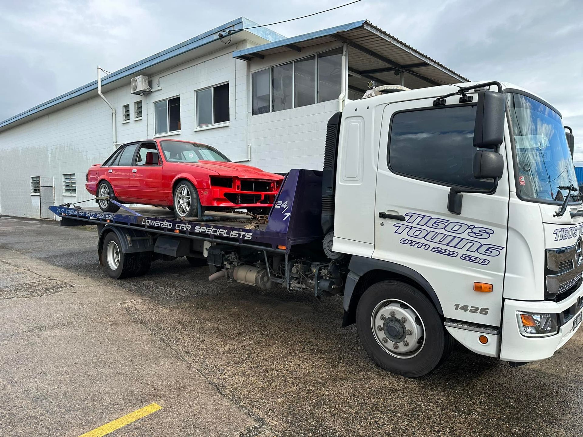 A Red Car Loaded Onto a White Tow Truck in Front of a White Building — Tigo’s Towing In Cairns City, QLD