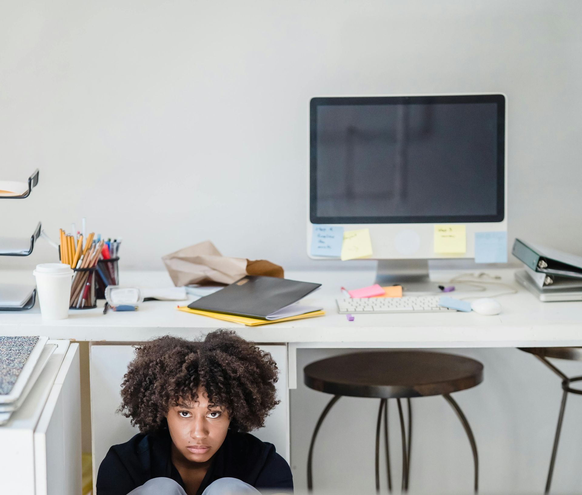 A woman is hiding under a desk in front of a computer.