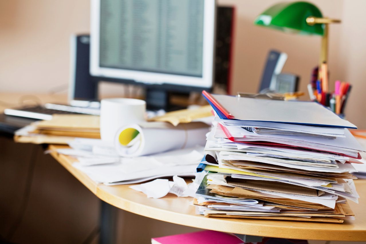 A desk with a stack of papers and a computer on it