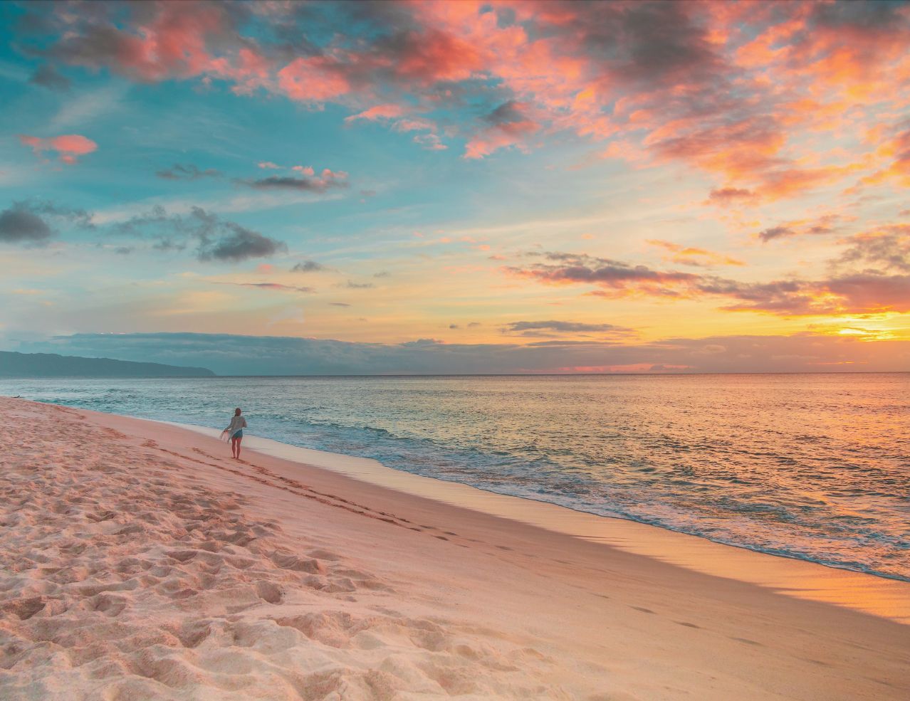 A person is standing on a beach at sunset.