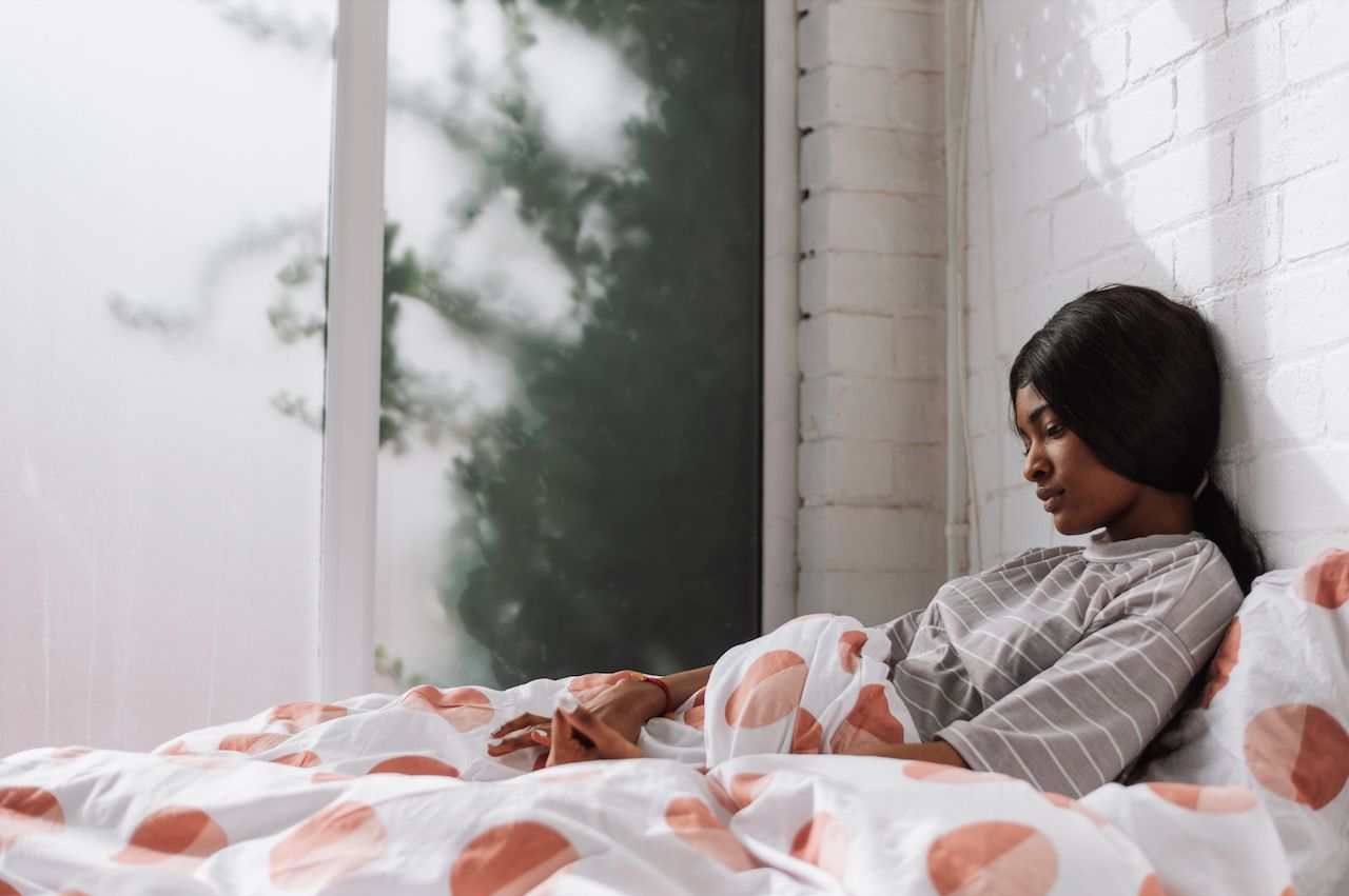 A woman is laying in bed looking out a window.