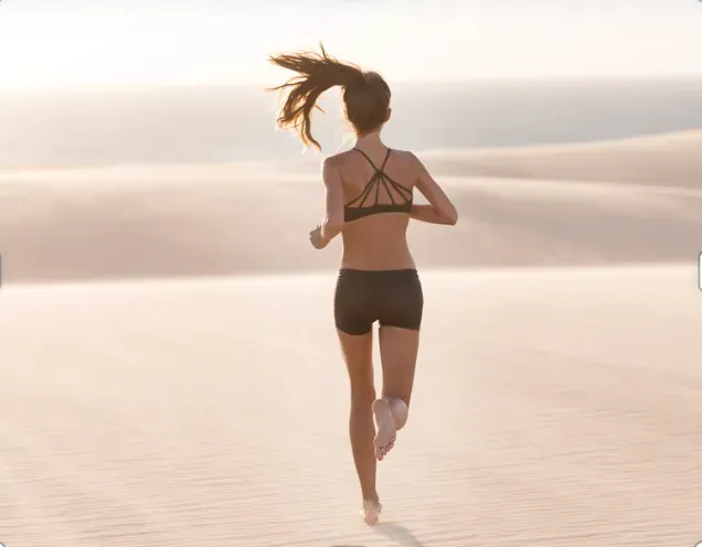 A woman is running on a sand dune near the ocean.