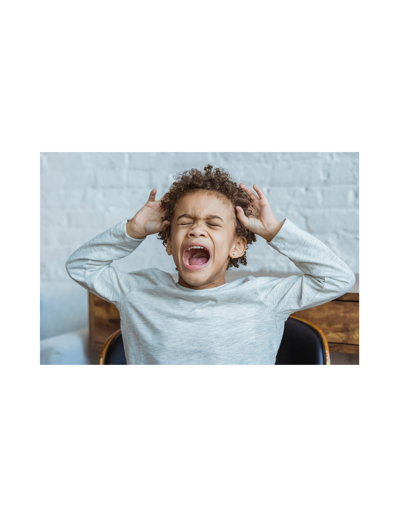 A young boy is screaming with his mouth open and covering his ears.