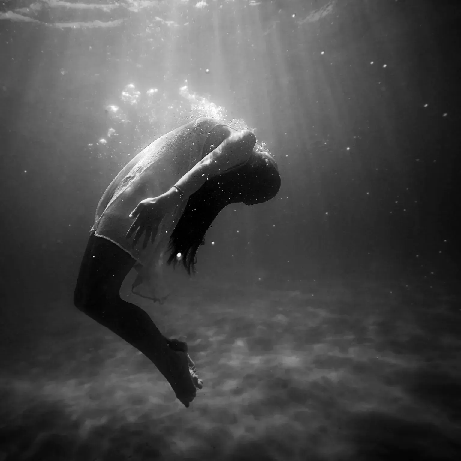 A woman is swimming underwater in a black and white photo.
