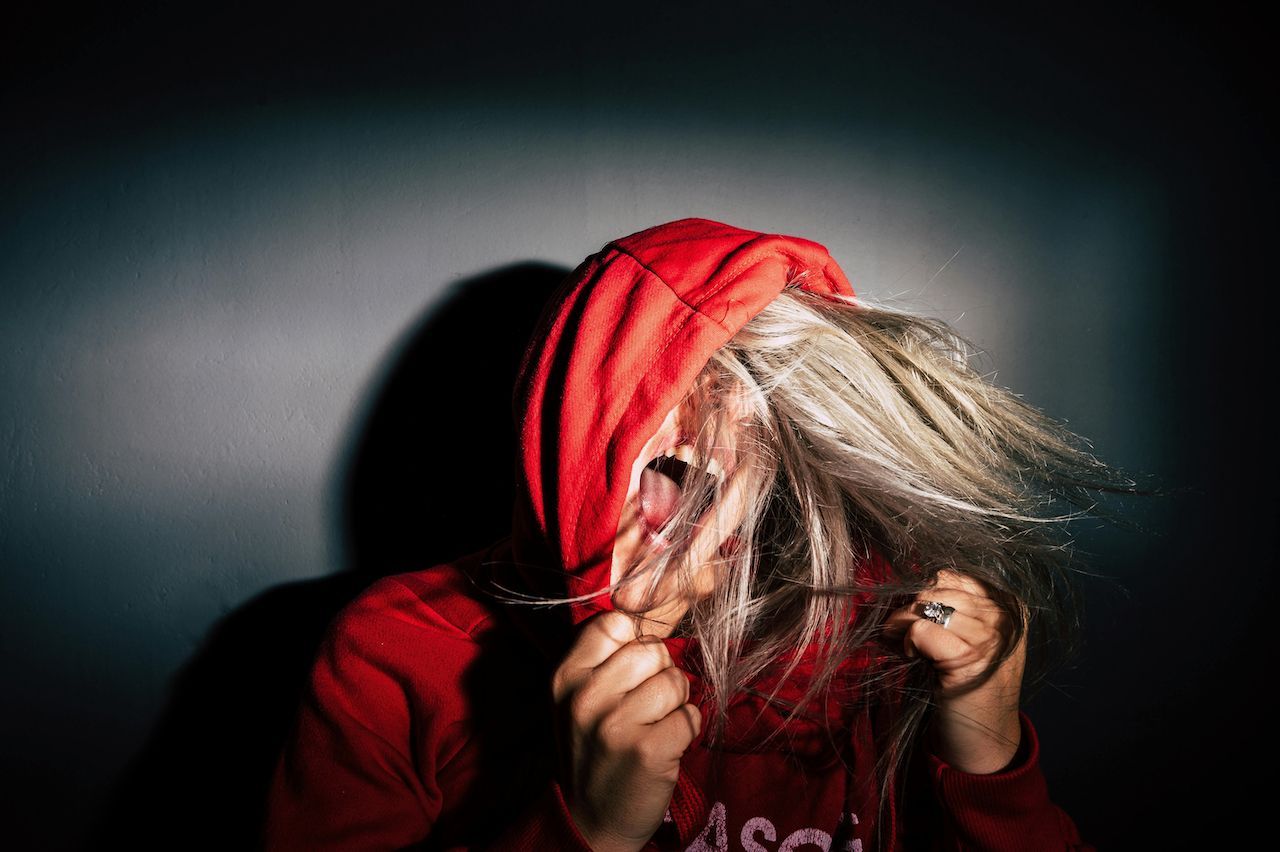 A woman in a red hoodie is holding her hair in front of her face.
