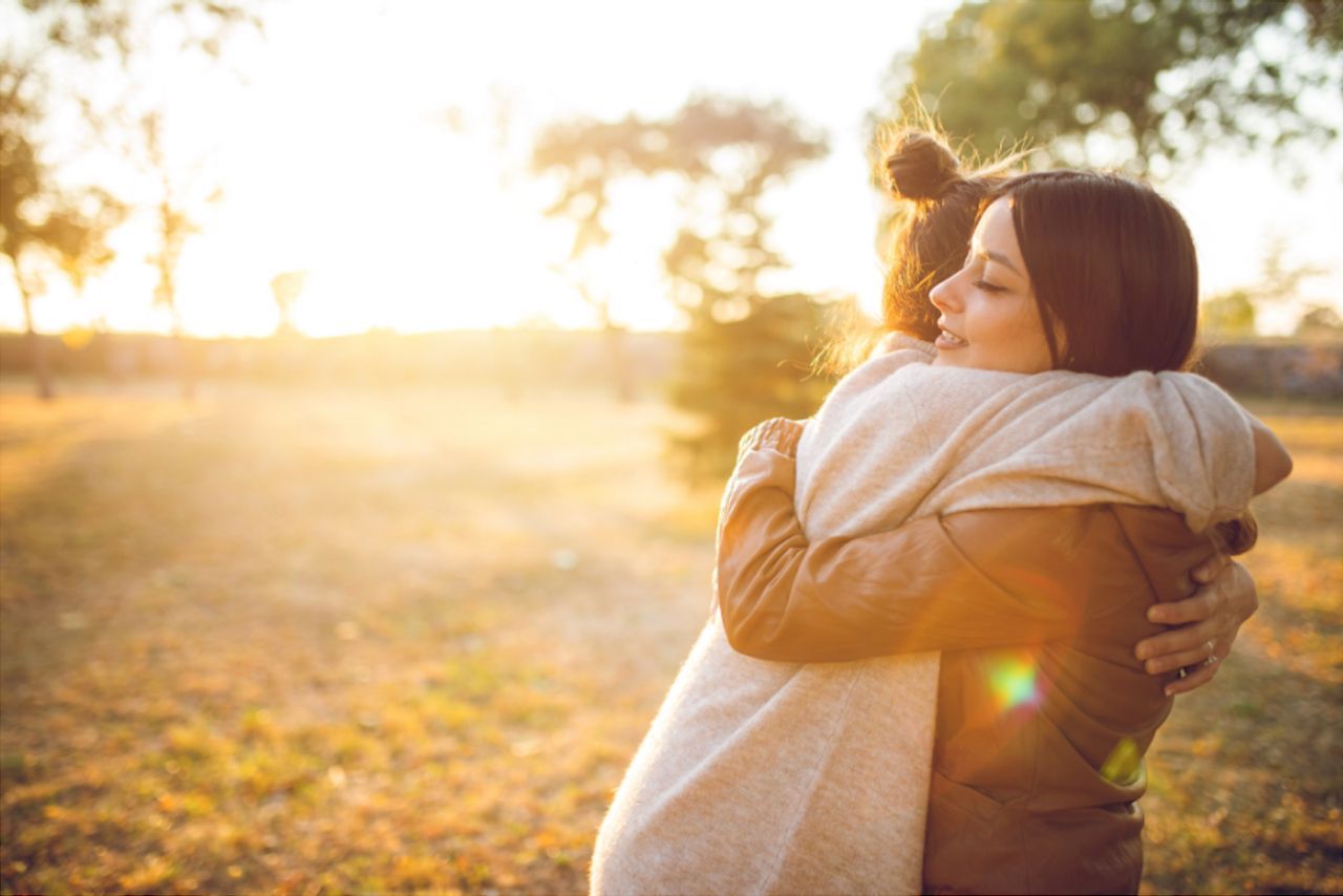 Two women embracing outdoors, bathed in warm sunlight.