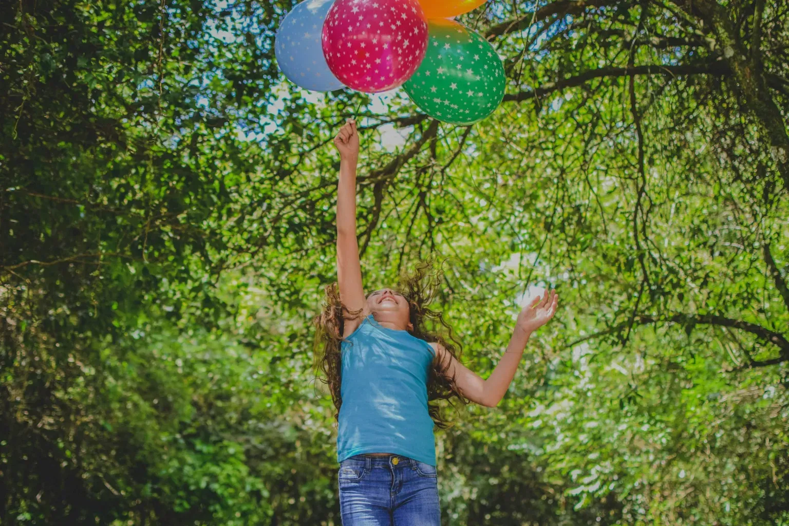A young girl is holding a bunch of balloons in the air.