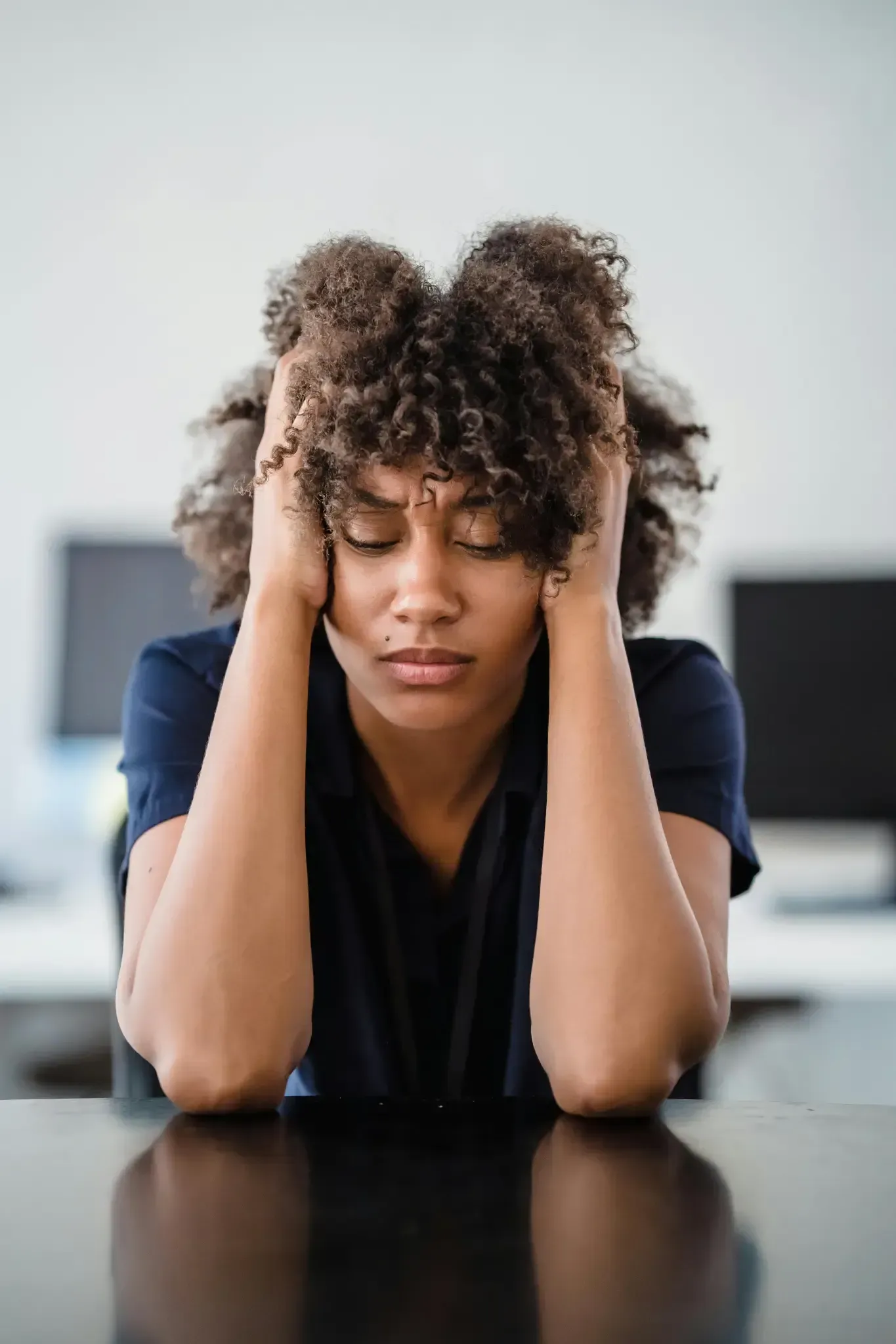 A woman is sitting at a table with her hands on her head.