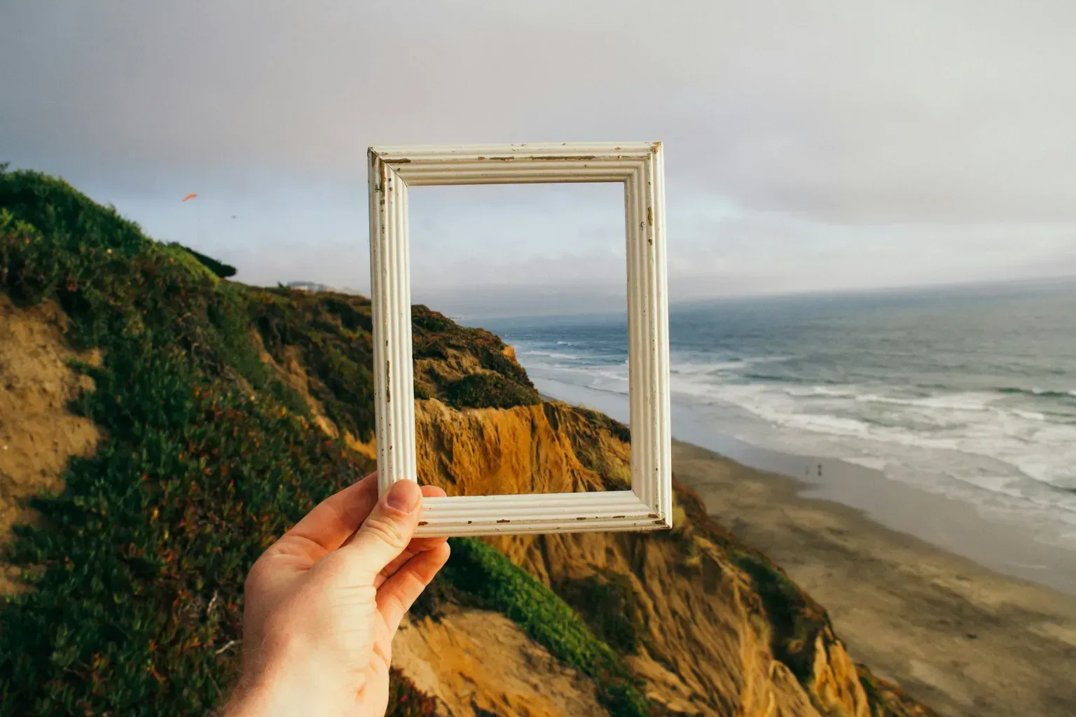 A person is holding a picture frame overlooking the ocean.