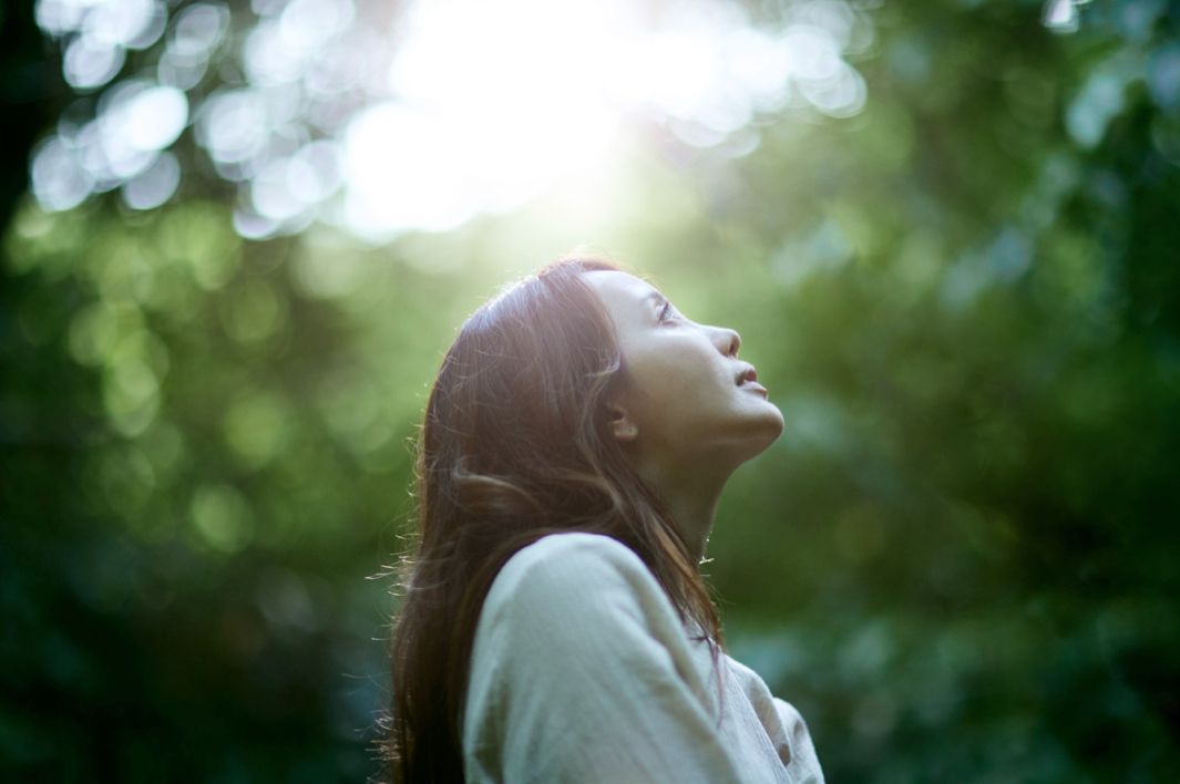 A woman is looking up at the sun in the woods.