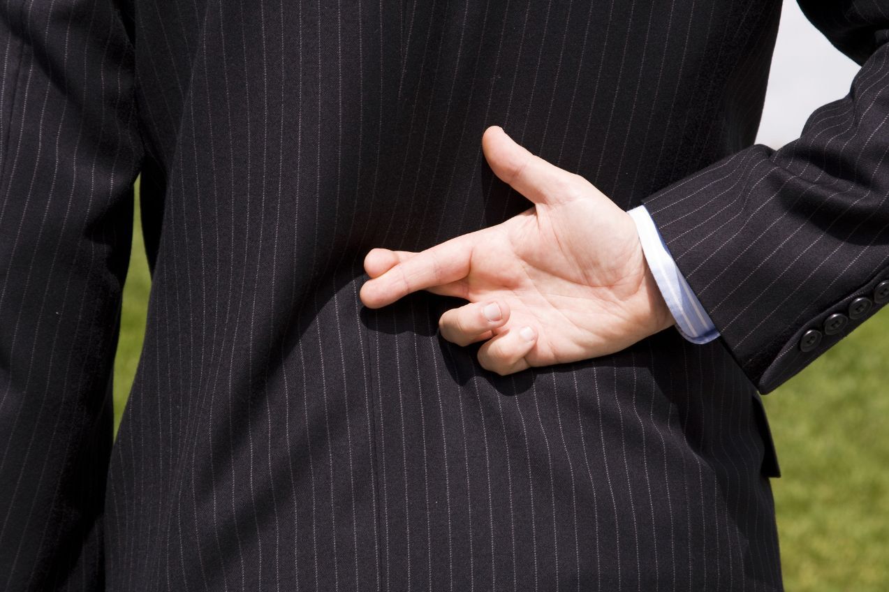 Person in a suit with crossed fingers behind their back, possibly lying.
