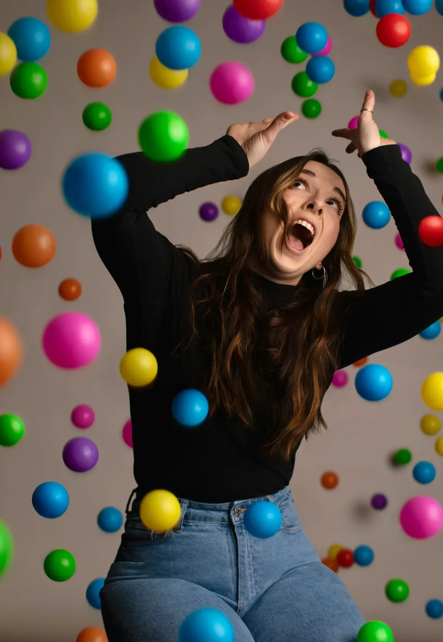 A woman is standing in front of a wall of colorful balloons.