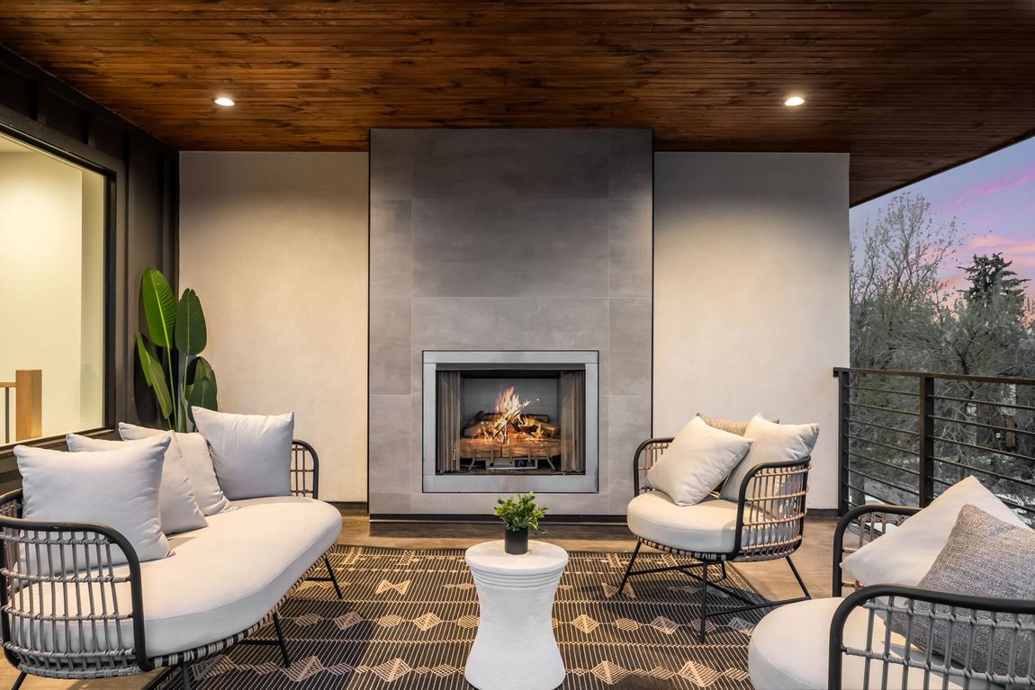 Outdoor living space with fireplace, seating, rug, and sunset.