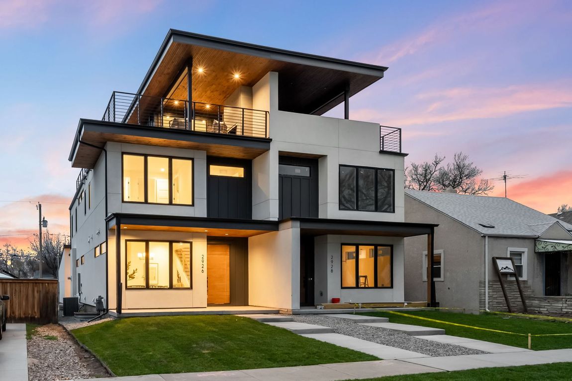 Modern multi-story home with balcony at dusk; white exterior, black accents.