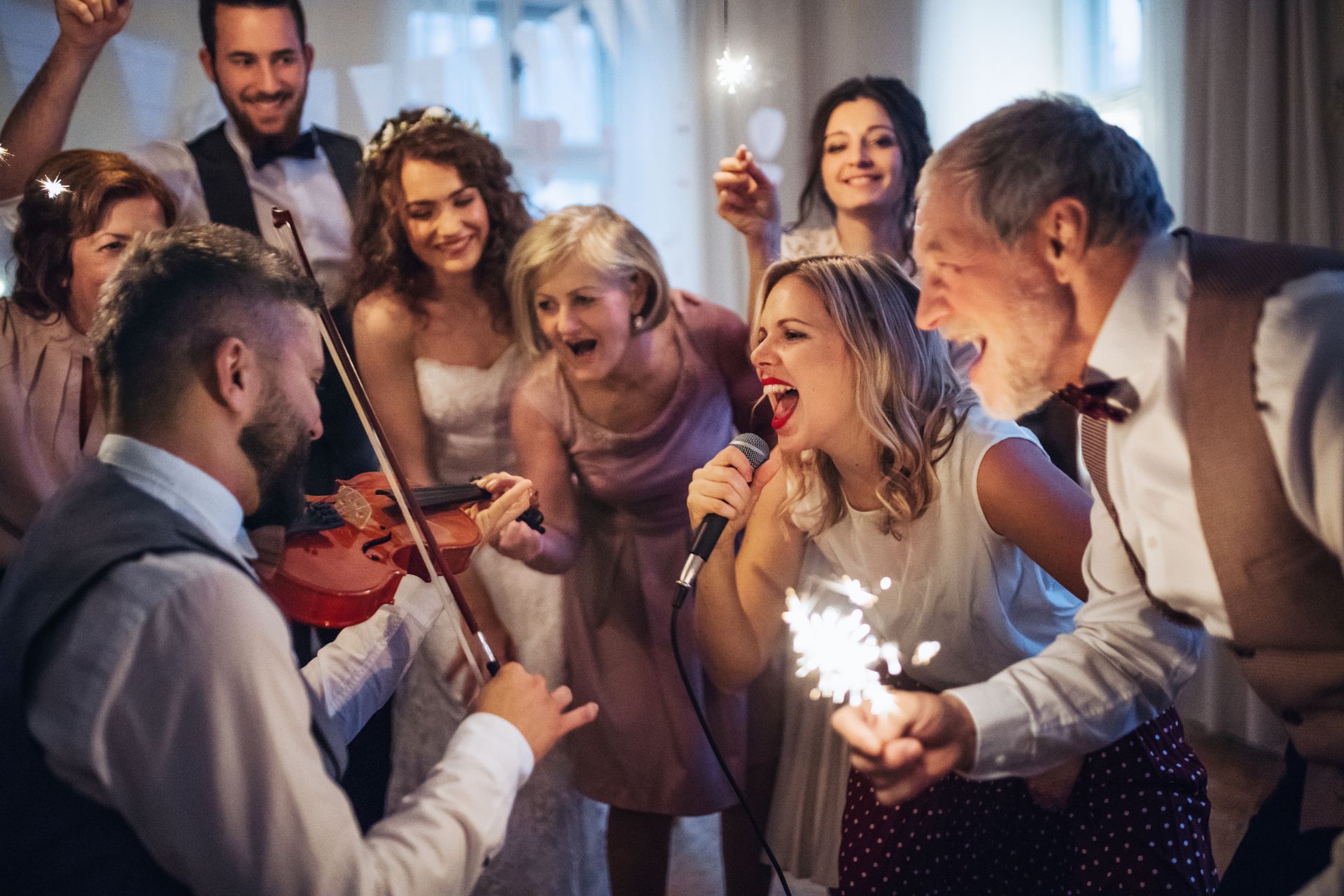 A man is playing a violin and a woman is singing into a microphone at a wedding reception.