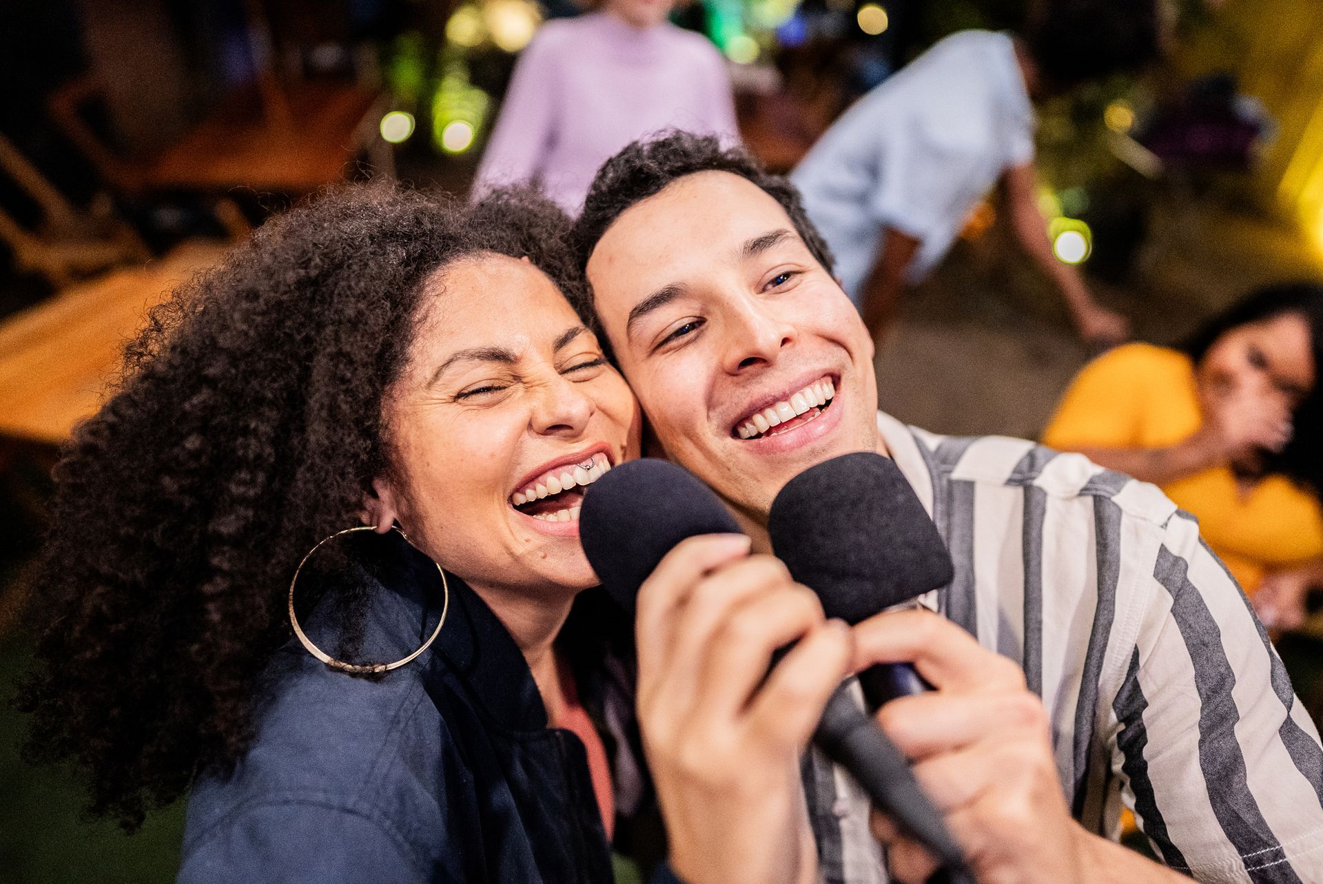 A man and a woman are singing into microphones at a party.