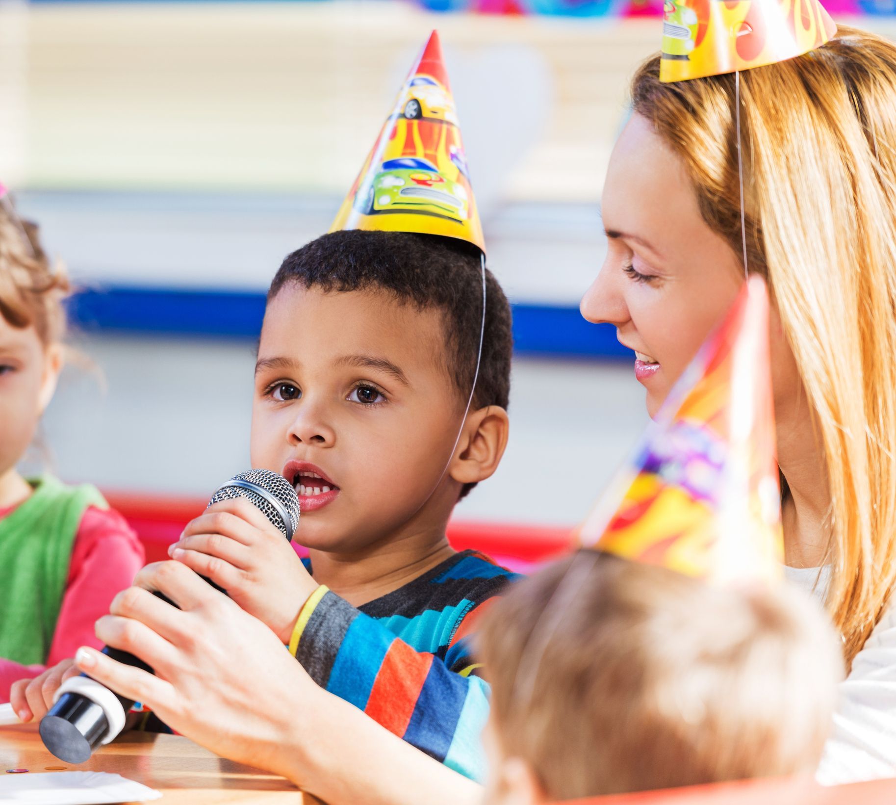 A little boy wearing a party hat is holding a microphone