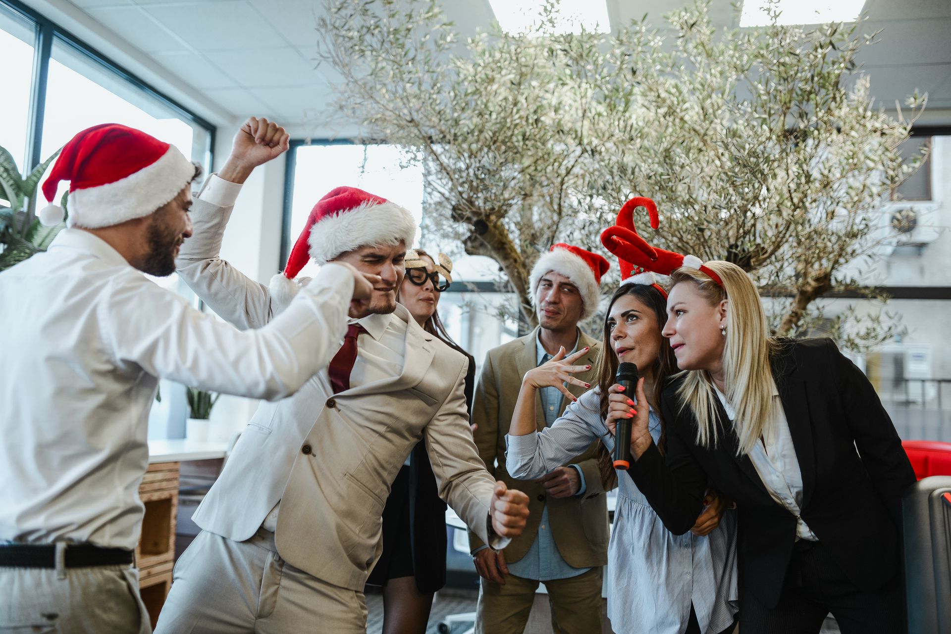 A group of people wearing santa hats are having a christmas party in an office.