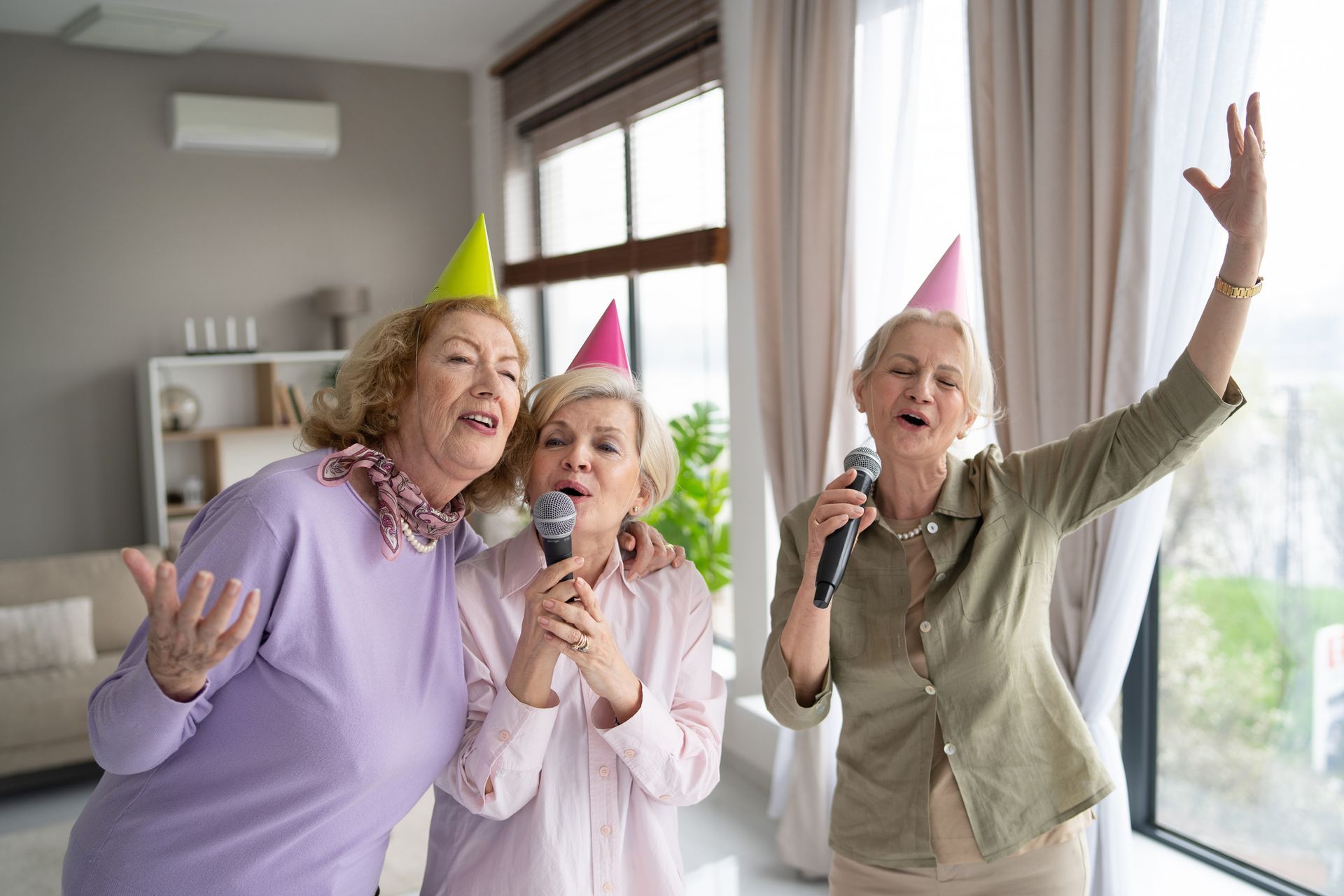 Three older women are singing into microphones at a party.