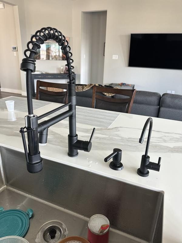 Black kitchen faucet with a pull-down sprayer, soap dispenser, and drinking water faucet on a white countertop.