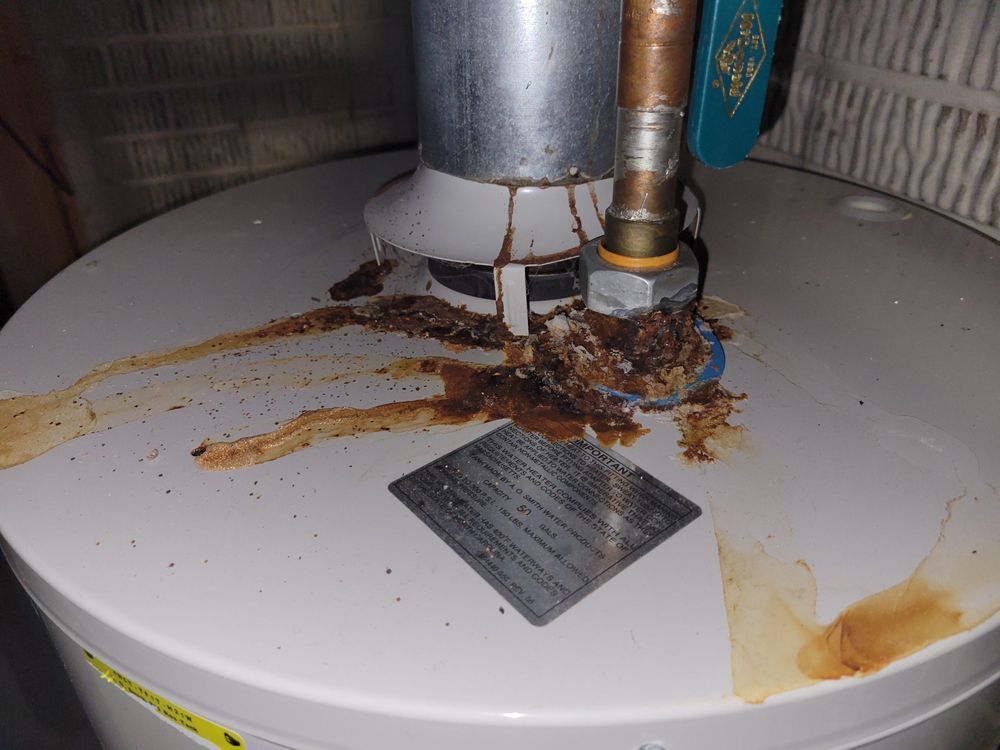 A water heater with brown, rust-colored leakage around the top fittings.