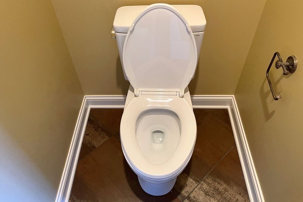 Toilet with the lid open in a small bathroom with brown tiled floor and tan walls.