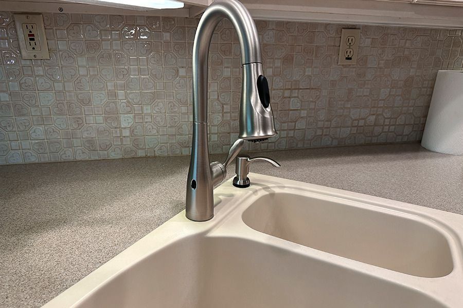 Stainless steel kitchen faucet over a double sink, with backsplash and soap dispenser.