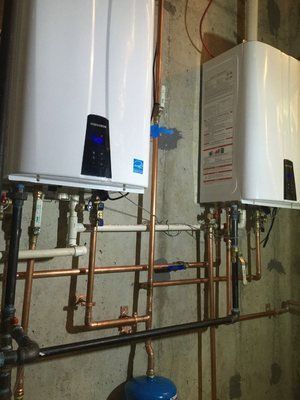 Two white tankless water heaters mounted on a concrete wall with copper piping.