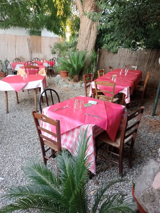 Tavoli da ristorante all'aperto apparecchiati con tovaglie rosa, circondati da piante e ghiaia.