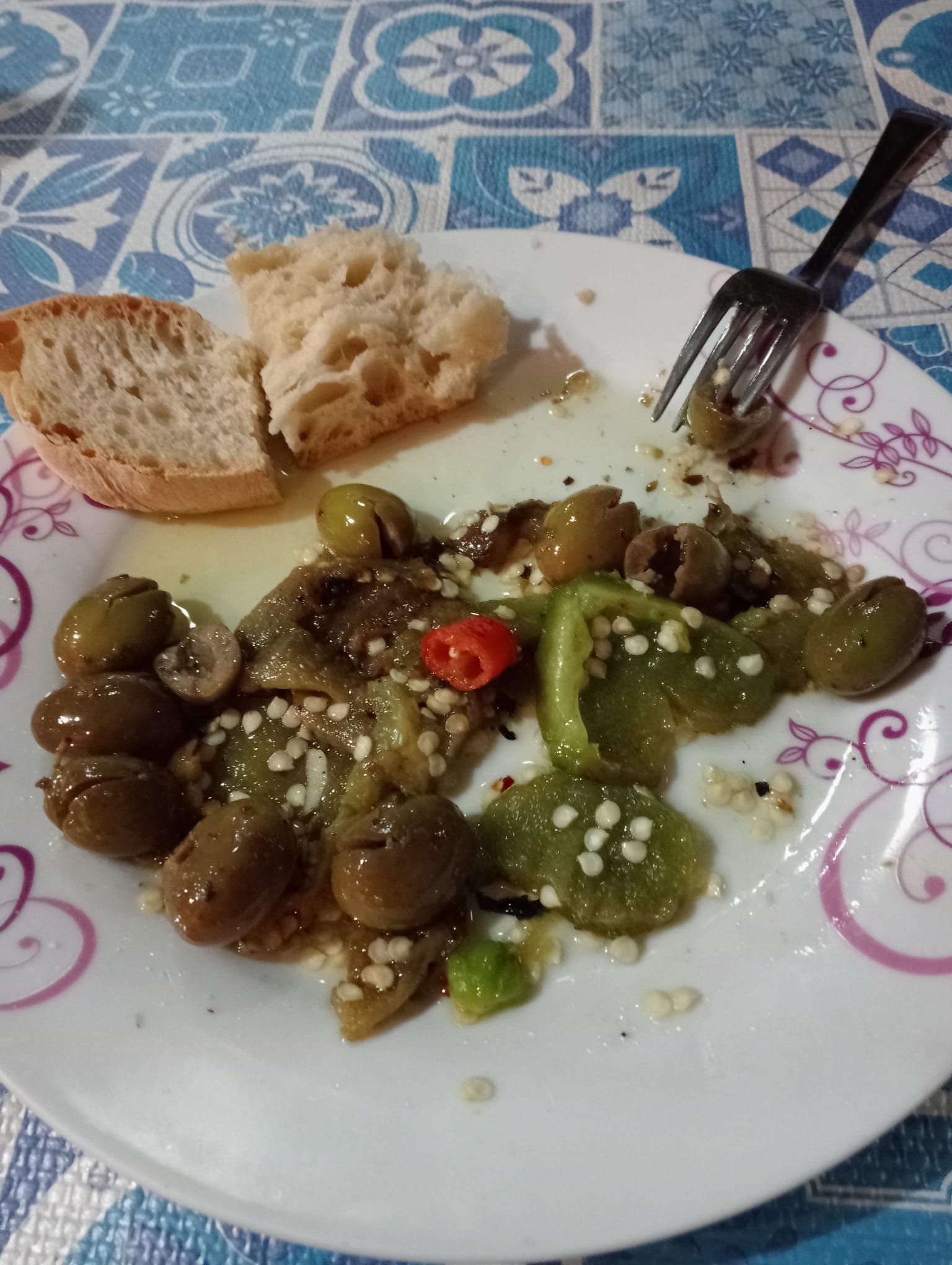 Piatto con olive, peperoni, pane e peperoncino, con una forchetta.