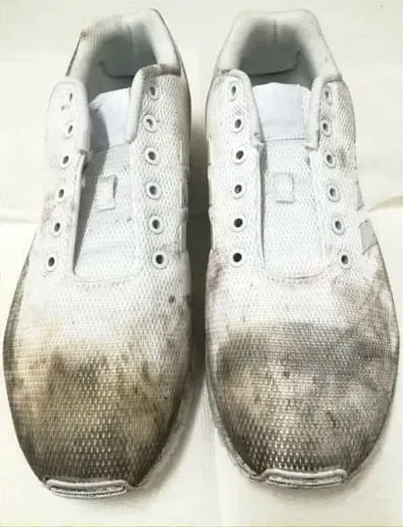 Un paio di scarpe da ginnastica bianche sporche, molto sporche sulle suole e sulla parte inferiore.