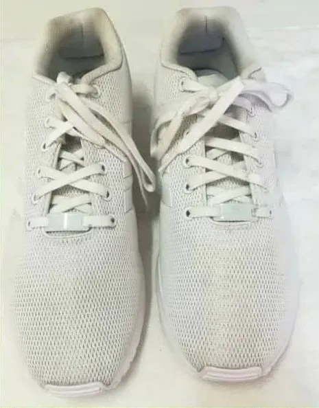 Un paio di scarpe da ginnastica bianche con lacci bianchi, appoggiate su una superficie bianca.