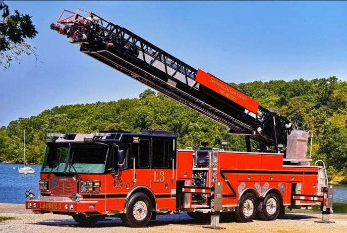 Red fire truck with extended ladder parked beside a lake on a sunny day