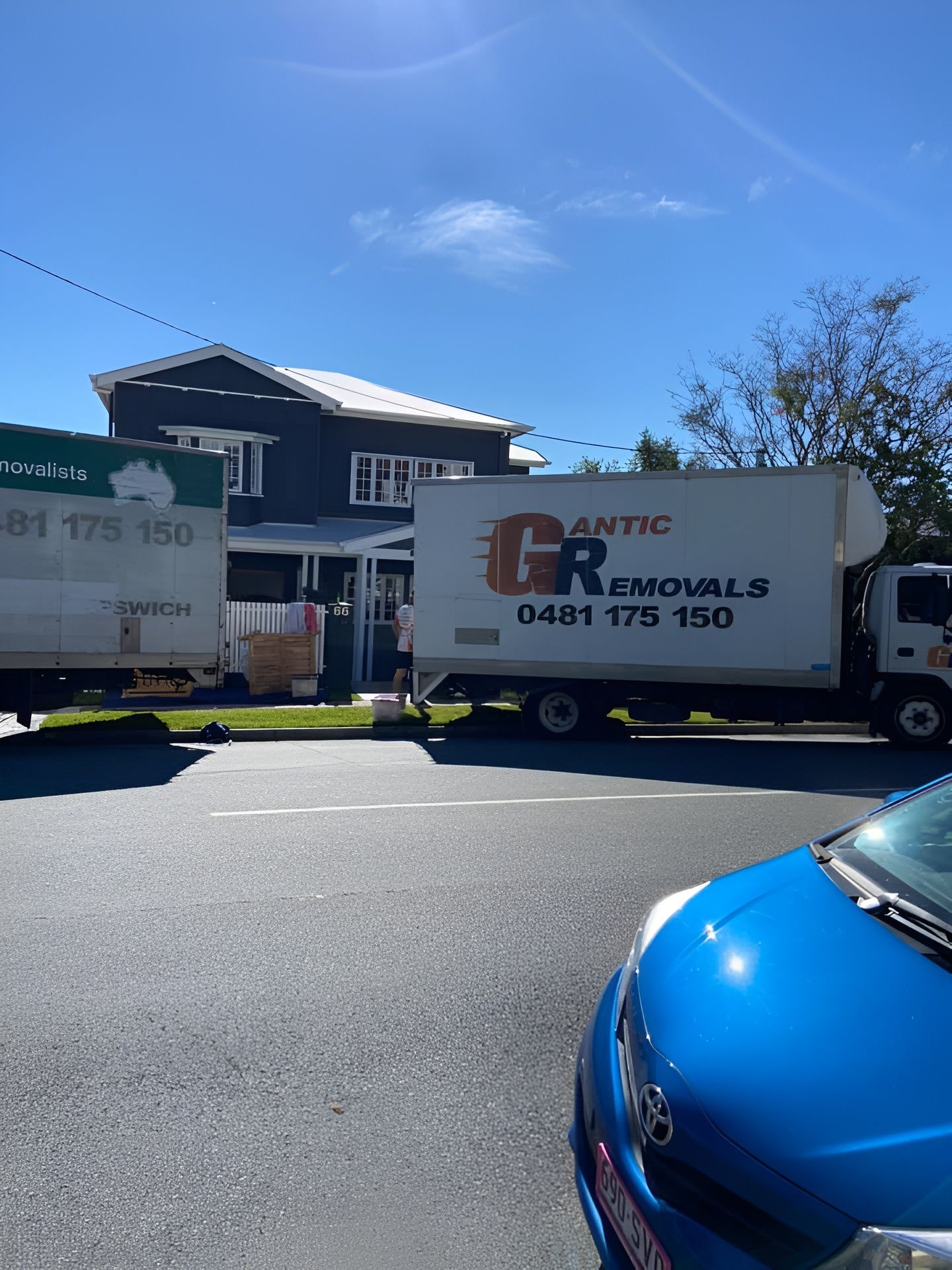 Moving trucks parked in front of a dark house on a sunny day. — Gantic Removals Ipswich in Ipswich, QLD